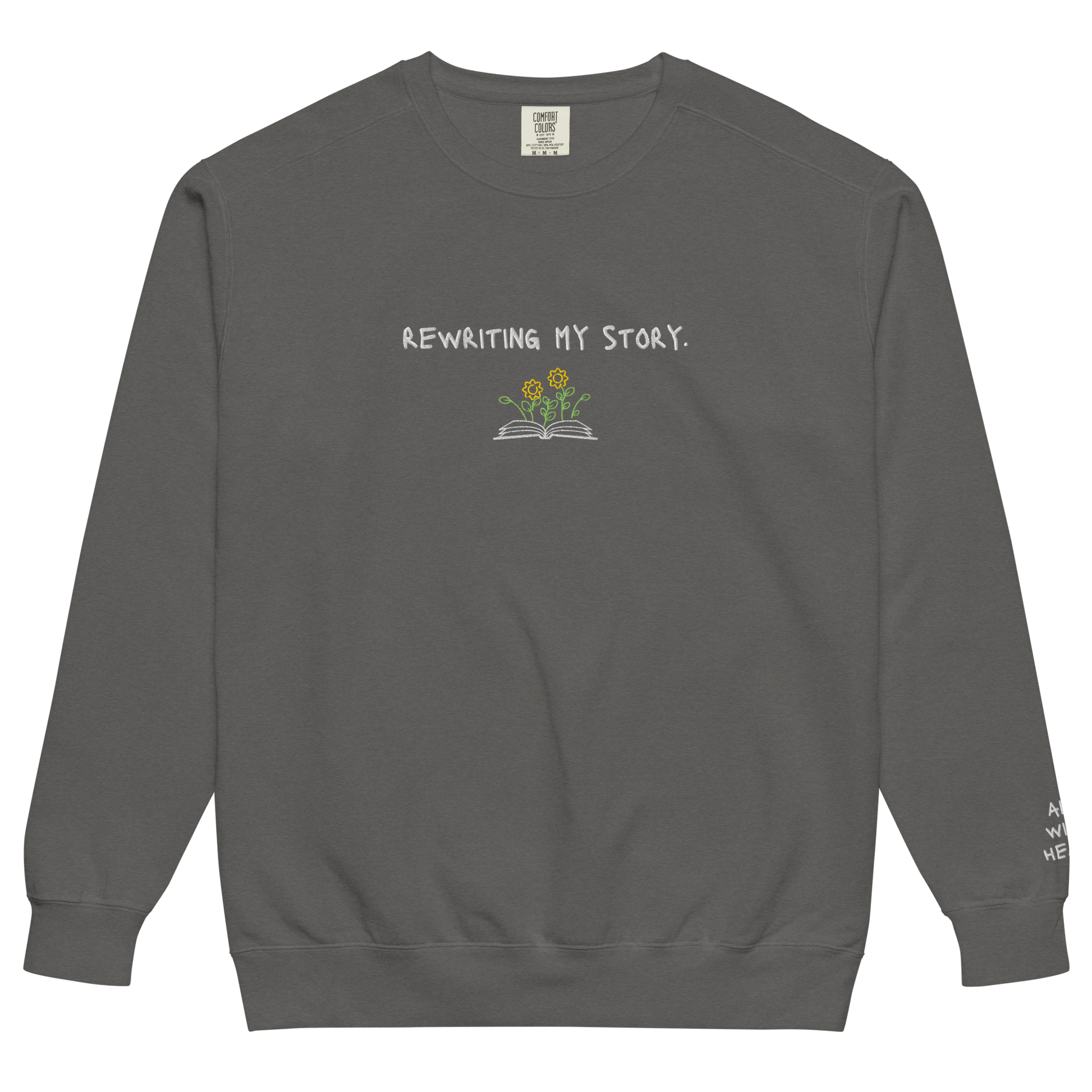 A black crewneck that says “Rewriting My Story” with an open book and flowers design.