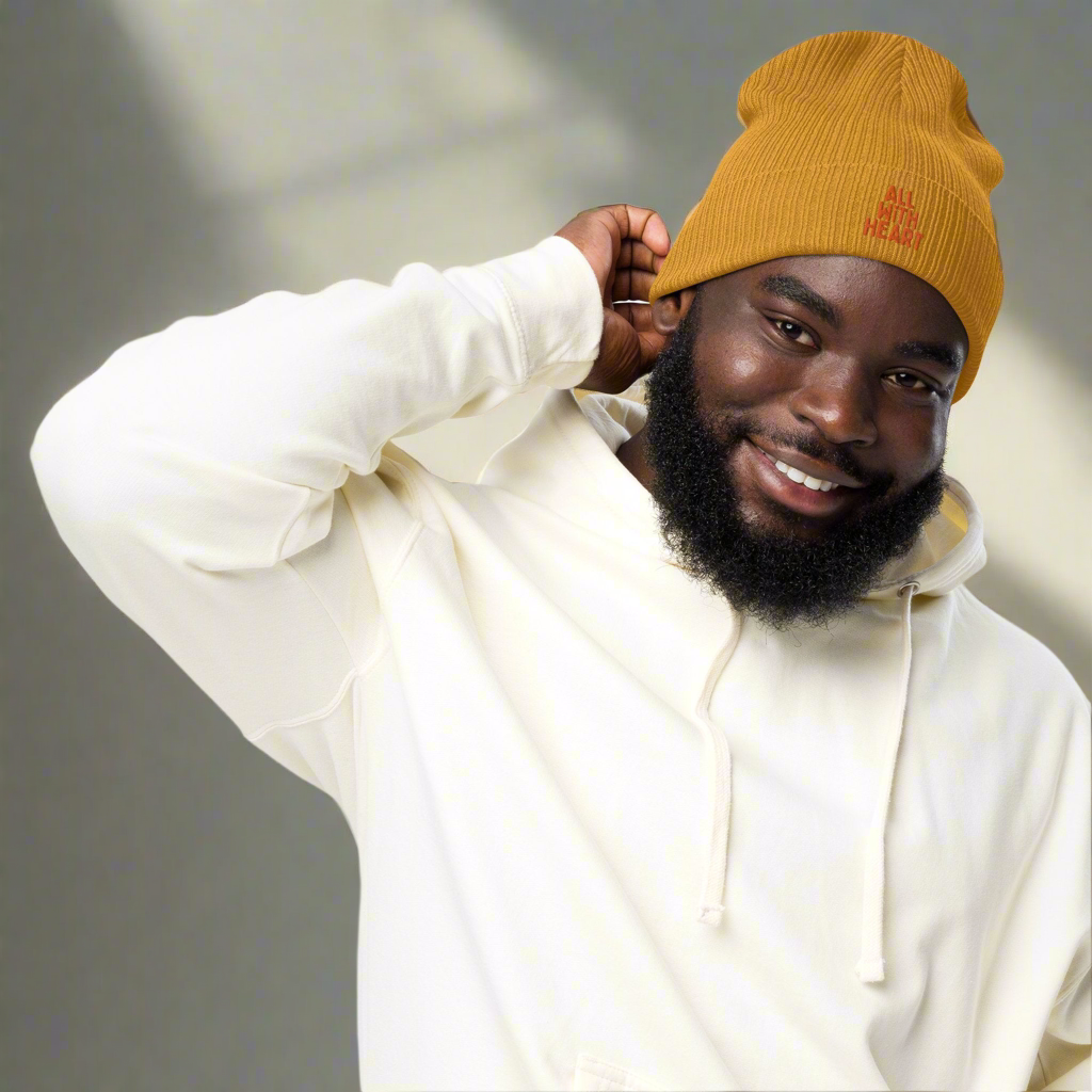 A man wearing a yellow organic beanie that says all with heart in orange text.