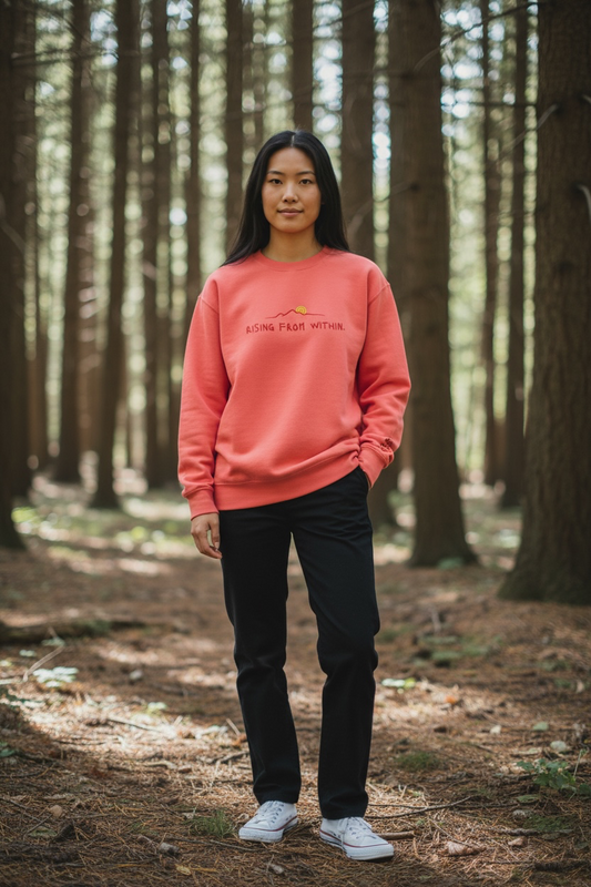 A woman wearing a bright red Crewneck that says “Rising From Within” with a mountain ridge design.
