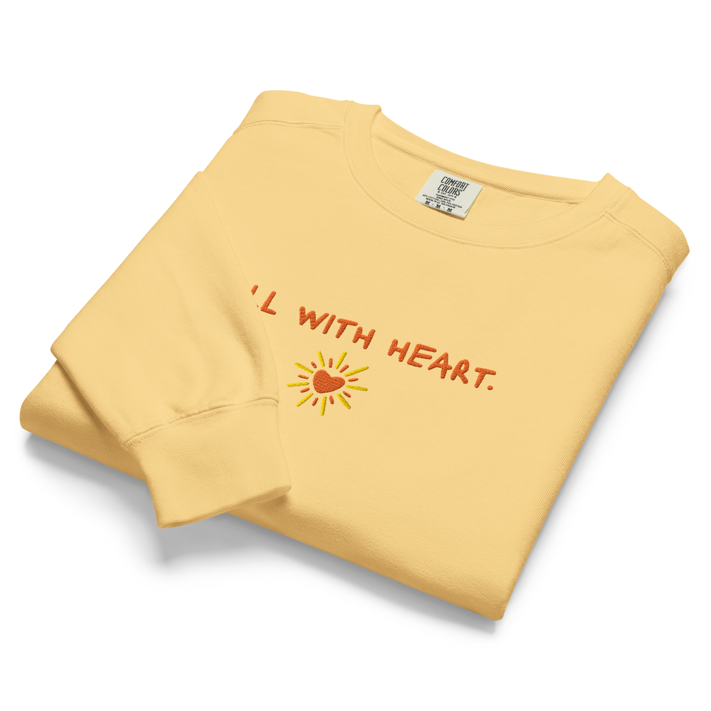 A close up of the folded “all with heart” Crewneck showcasing its heart sun design.