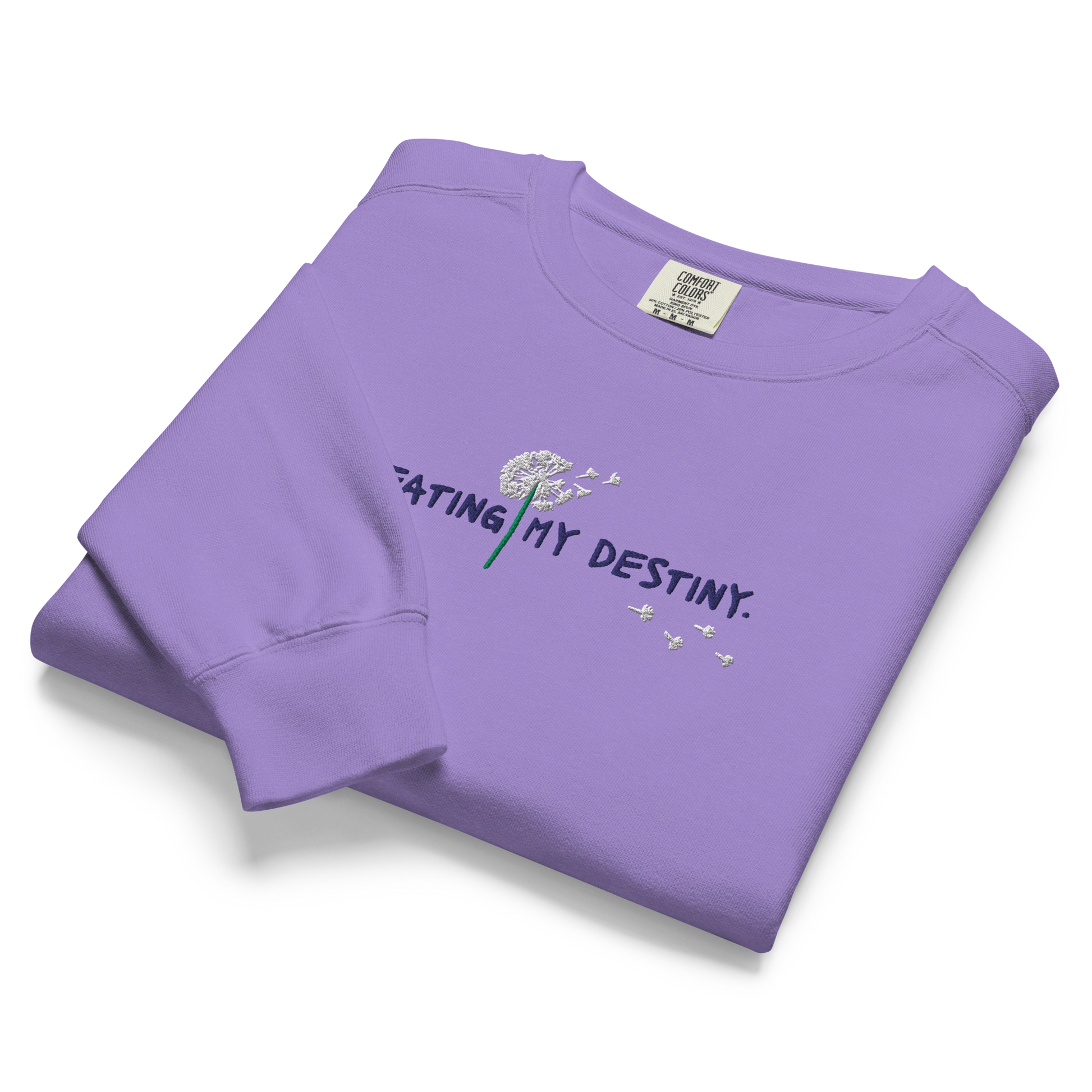 A folded purple Crewneck the says “Creating My Destiny” with a dandelion design.